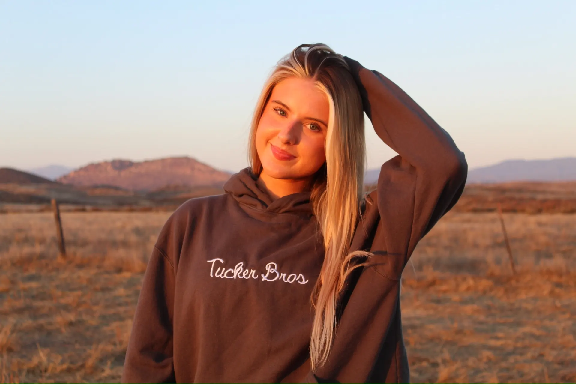 Woman in a Tucker Bros hoodie standing in open pasture at golden hour